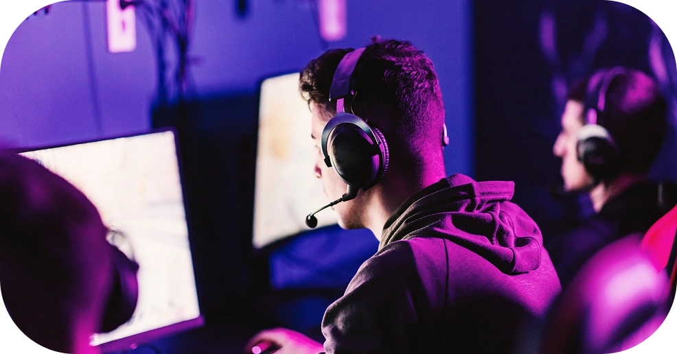 gracze e-sportowi w zestawach słuchawkowych grający przy komputerach w świetle neonów